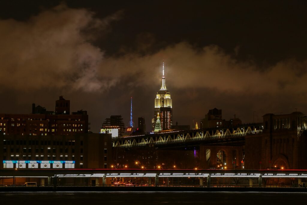 Captivating night view of the Empire State Building illuminated above the Brooklyn Bridge in New York City.
